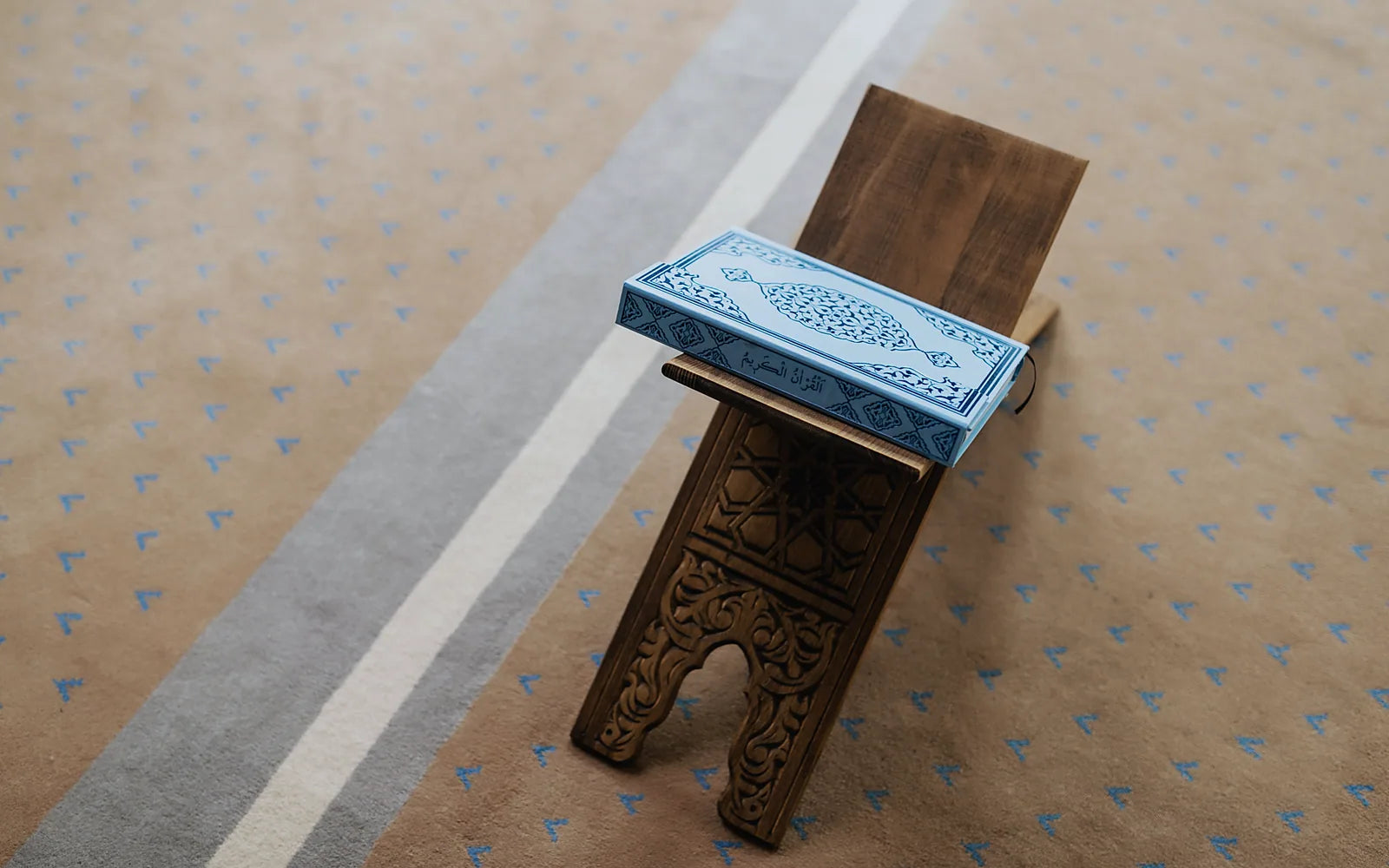 Porte-Coran en bois sculpté avec un Coran relié, posé sur un tapis de prière